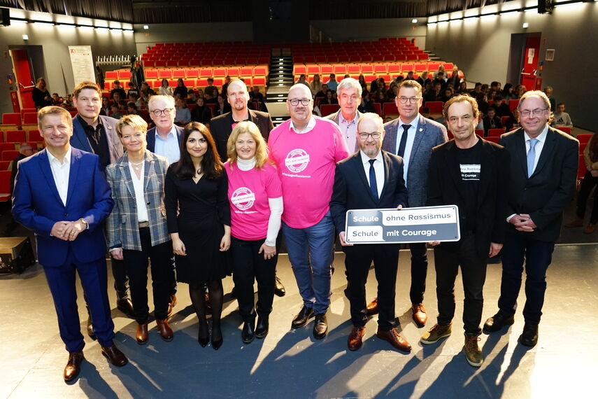 14 Personen stehen auf einer Bühne und halten ein Schild mit der Aufschrift 'Schule ohne Rassismus - Schule mit Courage' in den Händen.